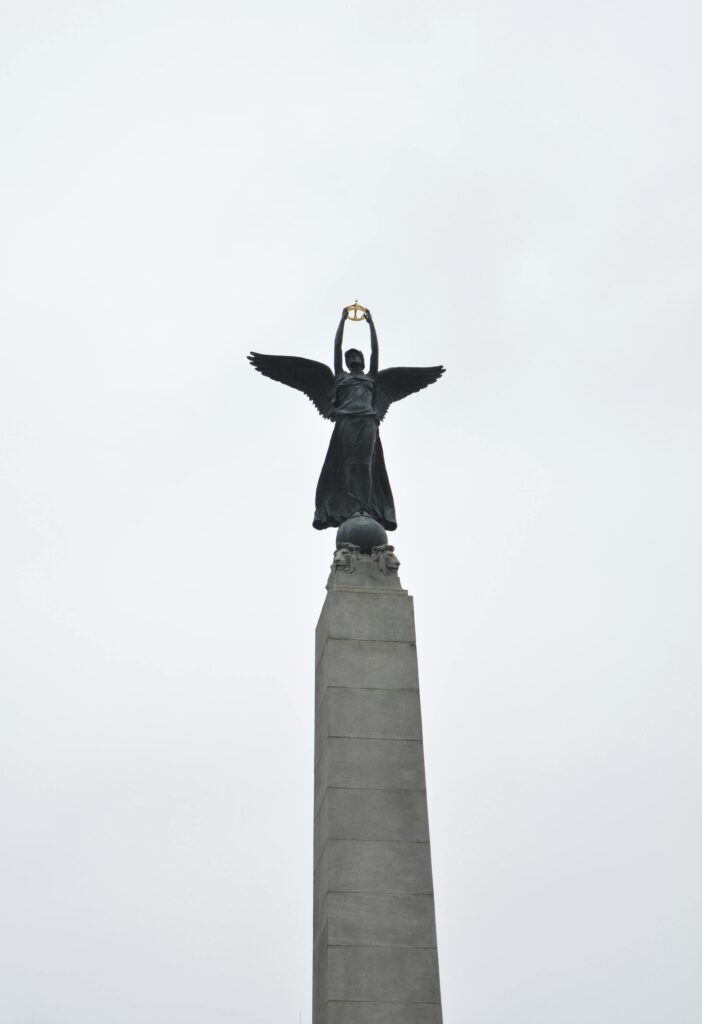 Low angle view of a monumental angel statue on a tall pillar, set against an overcast sky.